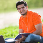Handsome Pakistani male sitting outdoors studying and listening to music.